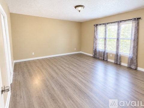 A spacious room with wooden flooring and a window with curtains.