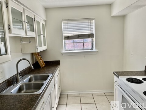 A kitchen with white cabinets and a window with blinds.