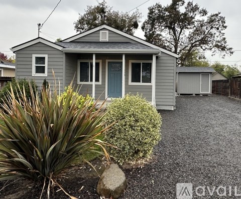 A grey house with a blue door and a gravel driveway.