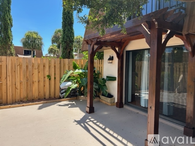 A wooden pergola is over a patio with a car parked in the background.
