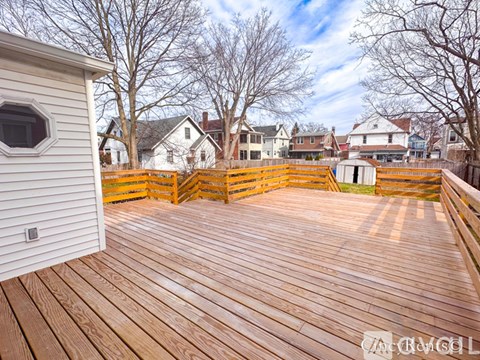 A wooden deck with a white house and trees in the background.