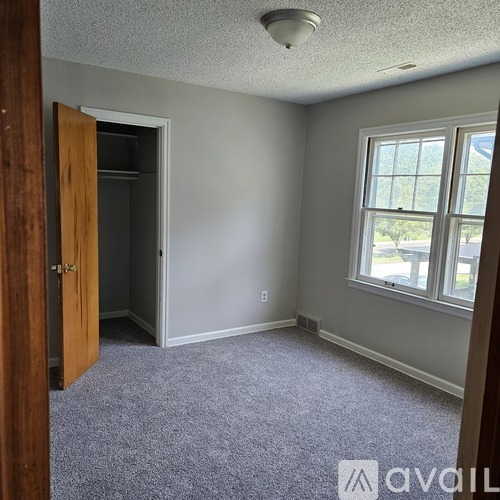 A room with a carpeted floor, a window, and a door.