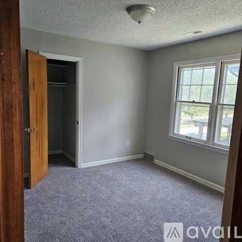 A room with a carpeted floor, a window, and a door.