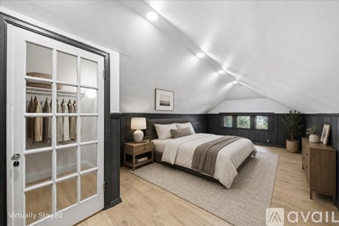 A bedroom with a bed, nightstand, and a wardrobe with clothes hanging.
