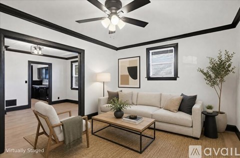 A living room with a white couch, a wooden chair, a glass coffee table, and a ceiling fan.