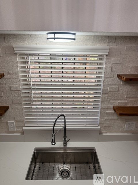 A kitchen sink with a faucet and a window with blinds.