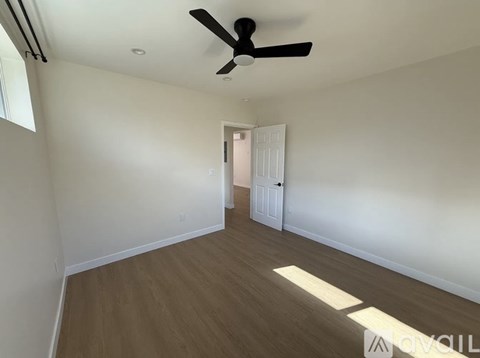 A room with a ceiling fan and light, wooden floors, and white walls.