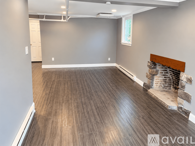 A room with wooden flooring and a fireplace on the right side.
