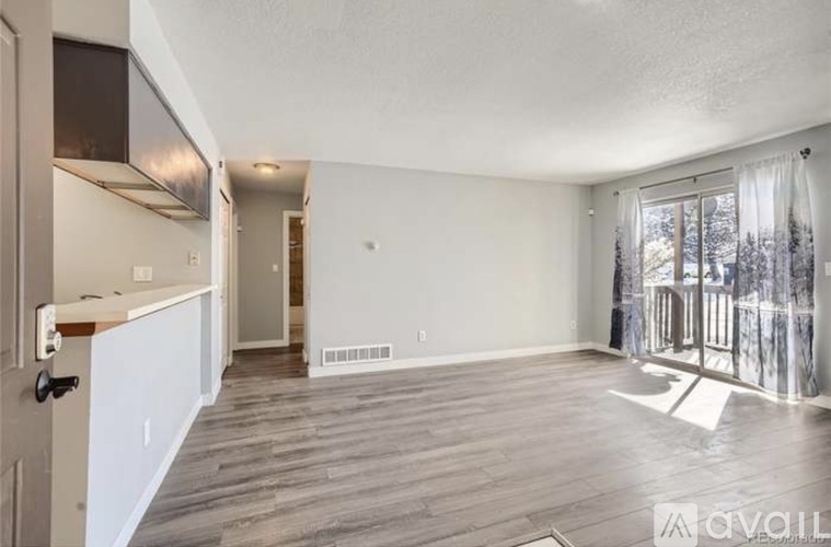 A spacious living room with wood flooring and a large window with a view of trees outside.