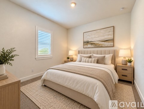 A bedroom with a large bed, two nightstands with lamps, and a framed picture on the wall.