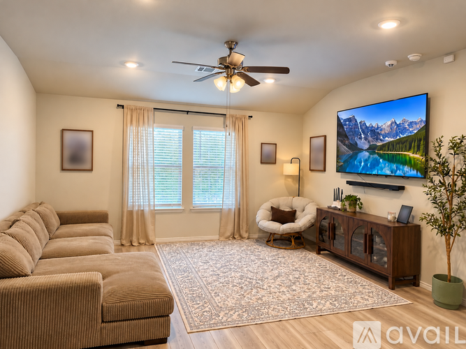 A living room with a brown sofa, a white chair, a wooden cabinet, and a large TV mounted on the wall.
