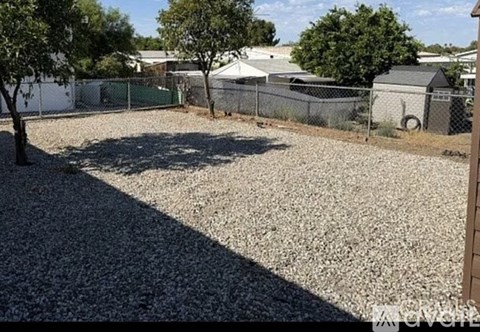 A gravel yard with a fence and trees.
