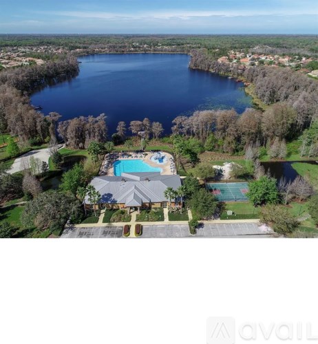 A house with a swimming pool is surrounded by trees and a large body of water.