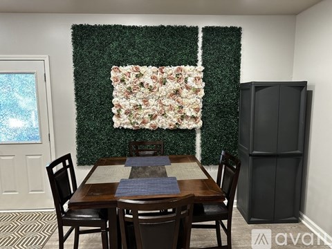 A dining room with a green hedge backdrop and a floral arrangement on the wall.