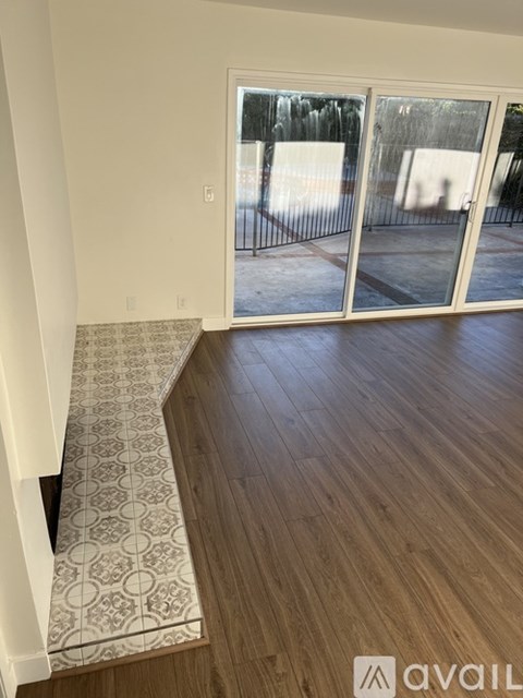 A room with a wooden floor and a tiled floor leading to a glass door.