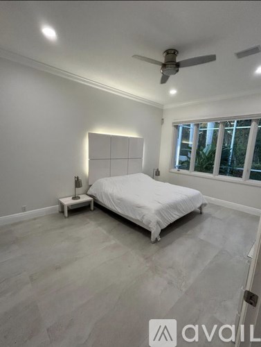 A bedroom with a bed, a small table with a lamp, and a window with a view of trees outside.