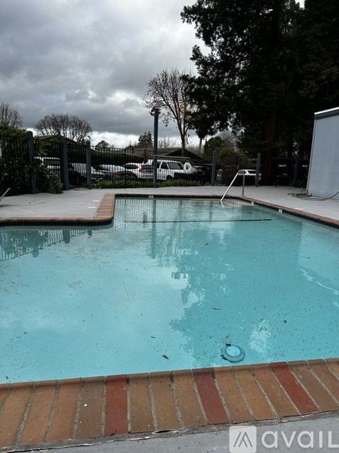 A pool with a brown brick border and a cloudy sky in the background.