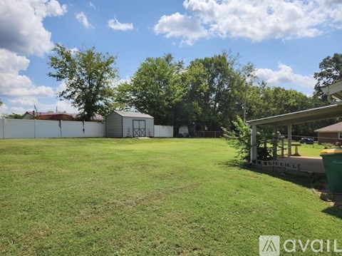 A grassy field with a shed and trees in the background.