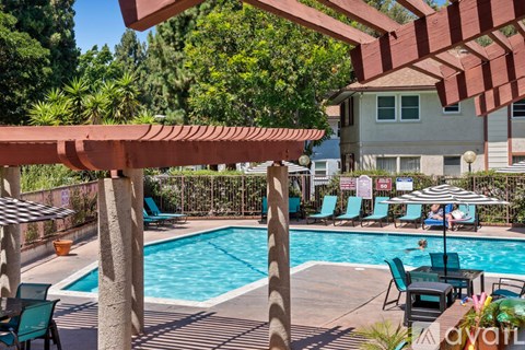 A pool area with a red pergola and lounge chairs.