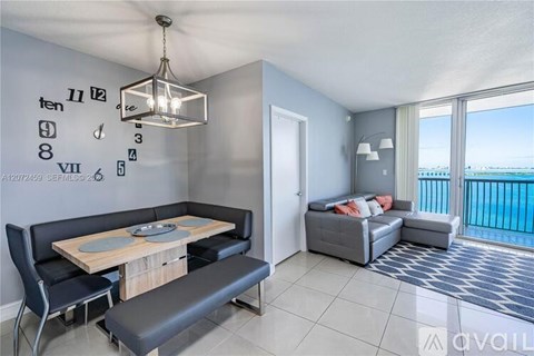 A living room with a dining table and a balcony overlooking the ocean.