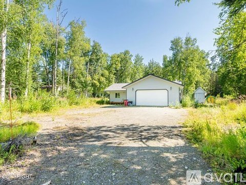A house with a garage is surrounded by trees and vegetation.