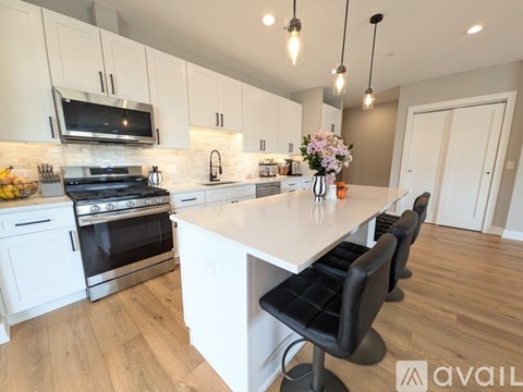A kitchen with white cabinets and a large island with black chairs.