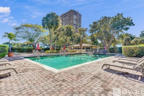A pool surrounded by trees and chairs with a building in the background.