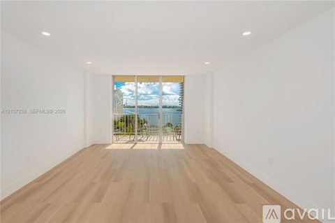 A spacious room with wooden flooring and a view of a cityscape through a window.