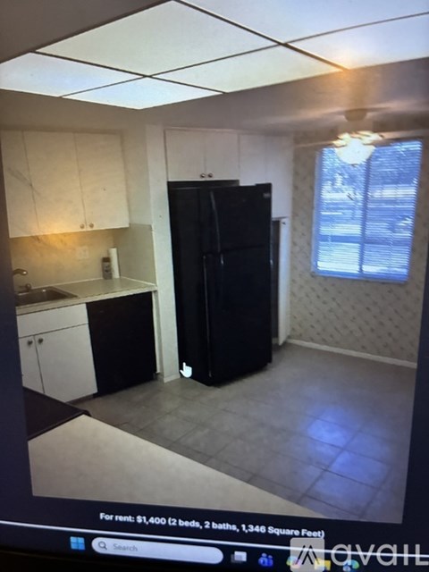 A black refrigerator in a kitchen with white cabinets.