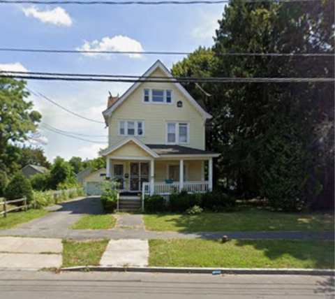 A yellow house with a white porch and a green lawn.
