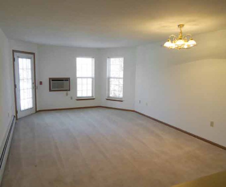 an empty living room with a wood floor and a chandelier