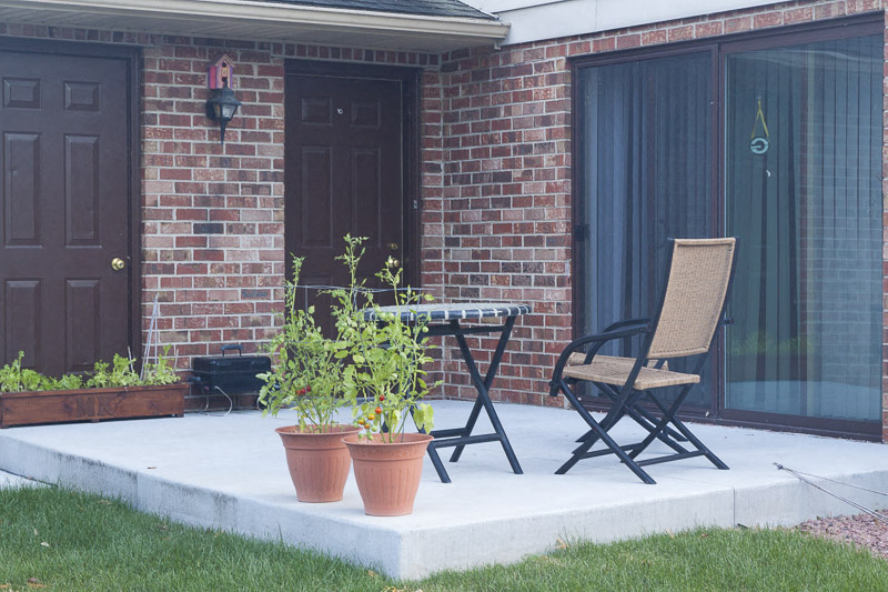 a patio with a chair and a table and pots of plants