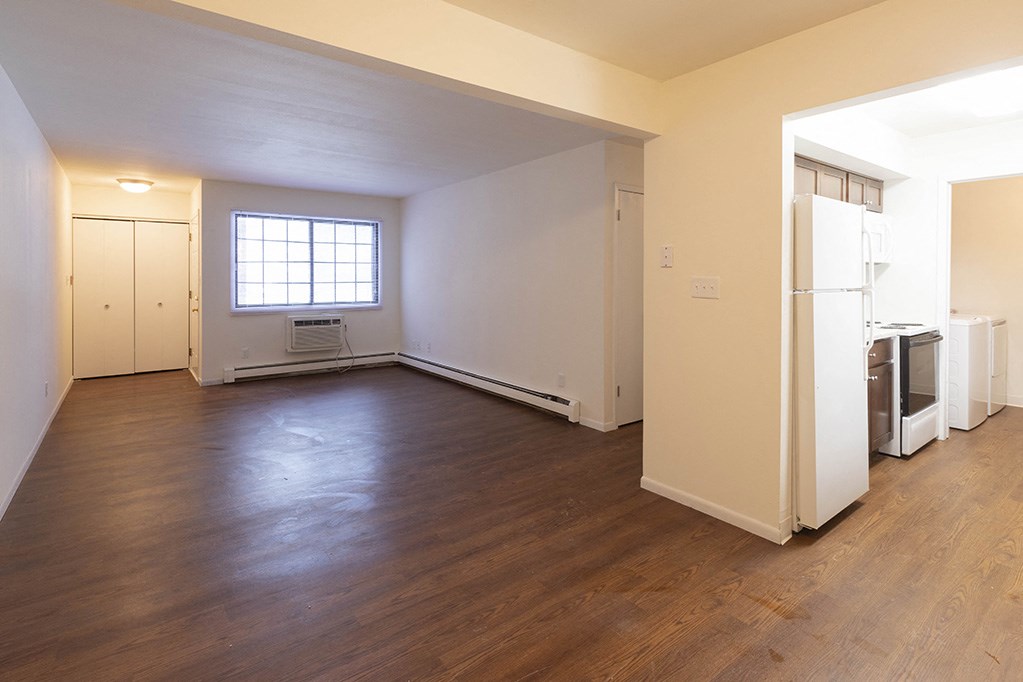 an empty living room with a refrigerator and a window
