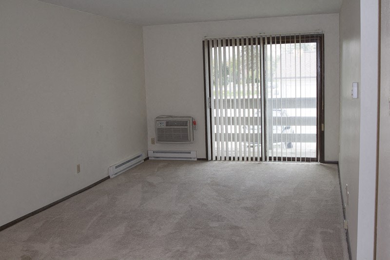 an empty living room with a window and a heater on the floor