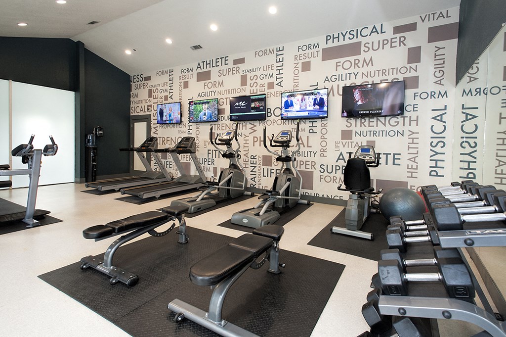a gym with weights and televisions on a wall