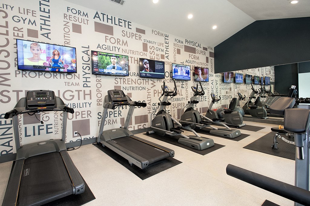 a gym with treadmills and televisions on the wall