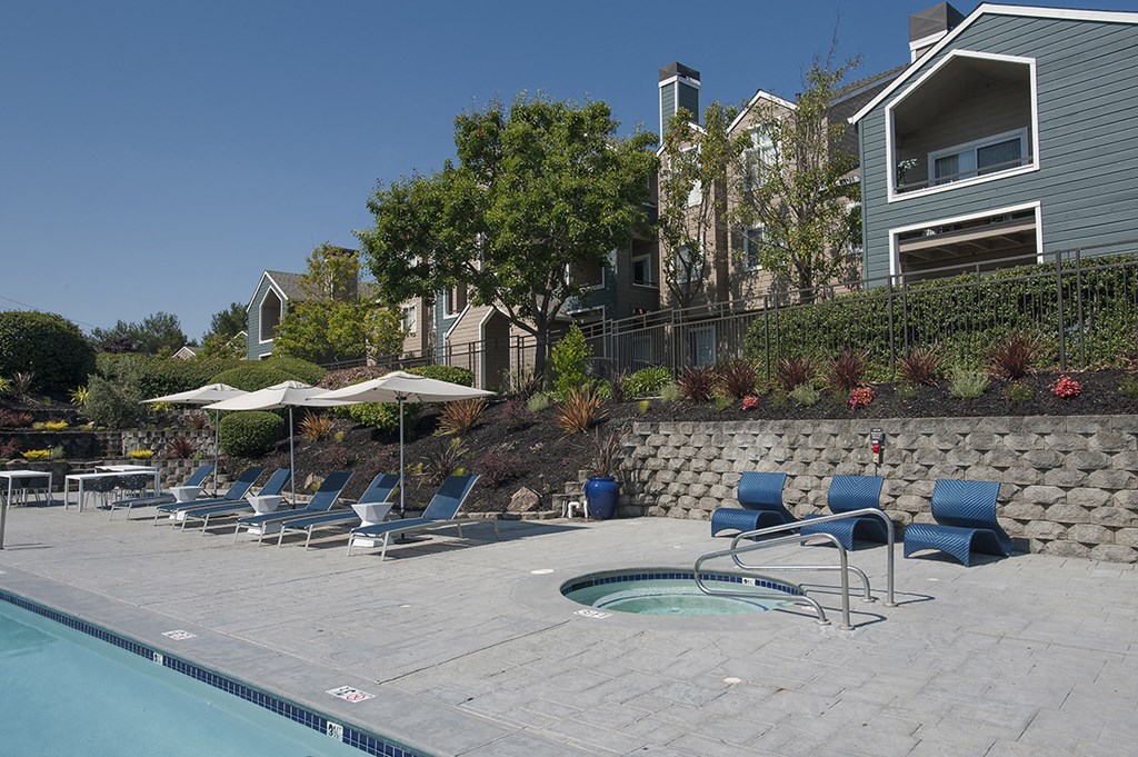 a swimming pool with chairs and umbrellas in front of a house