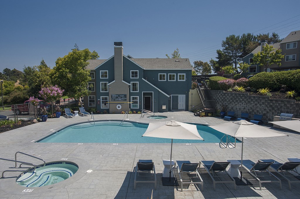 a pool with chairs and umbrellas and a house in the background