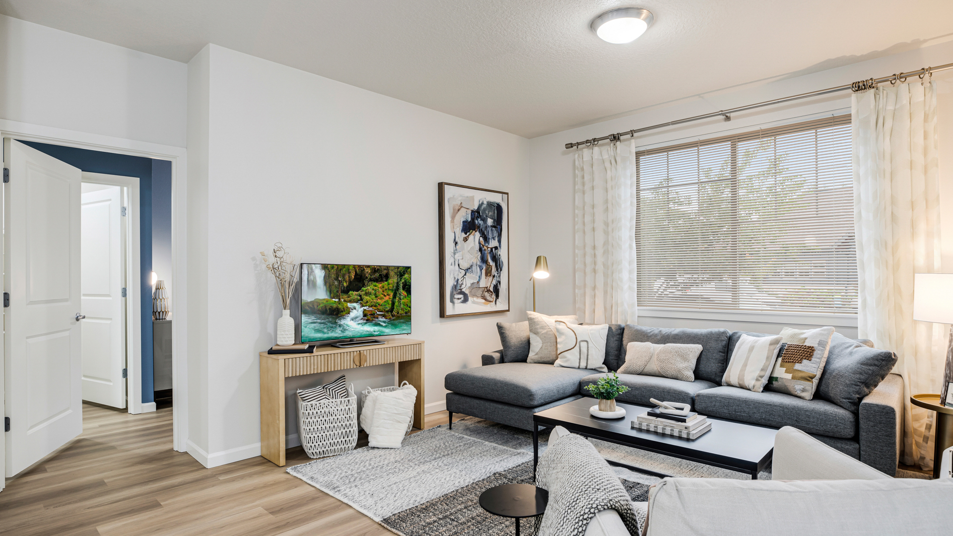 A living room with a grey couch, a coffee table, and a painting on the wall.