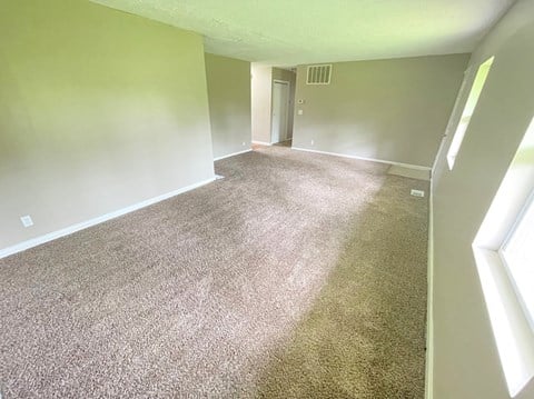 an empty room with a carpeted living room and a door to a hallway