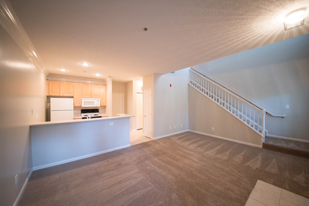 an empty living room with a kitchen and stairs