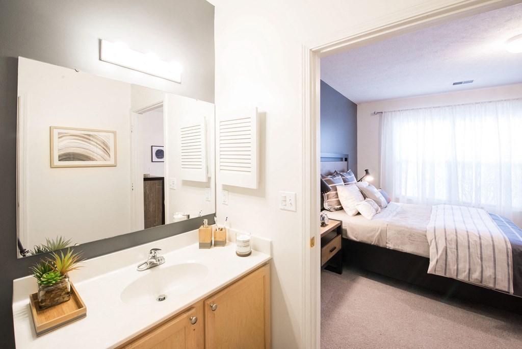 a bedroom with a large bed and a bathroom with a sink and a mirror