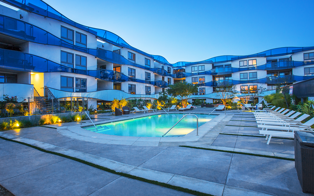 an apartment building with a pool and chairs at night