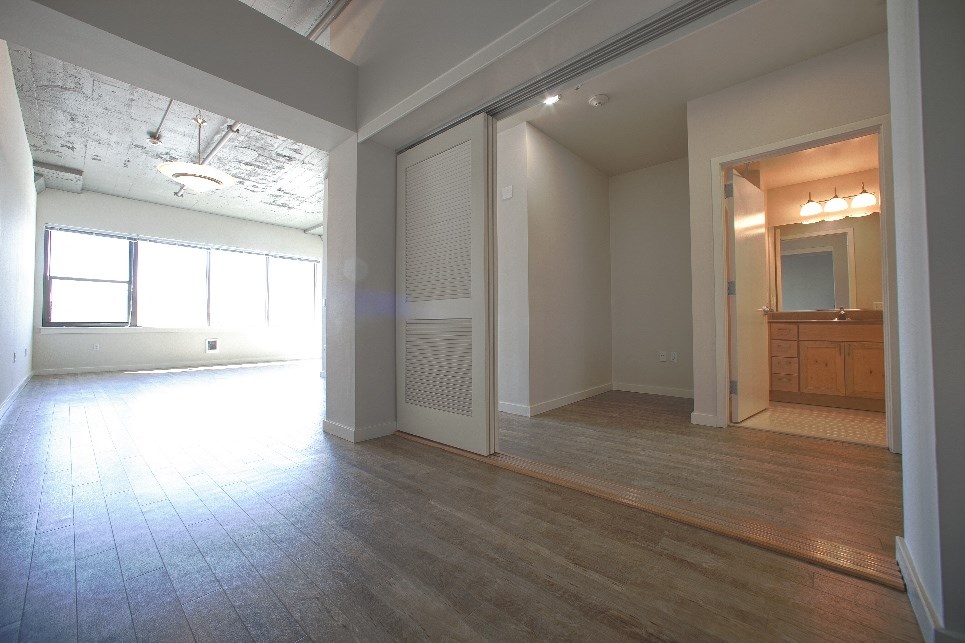an empty living room with a wood floor and a door to a bathroom