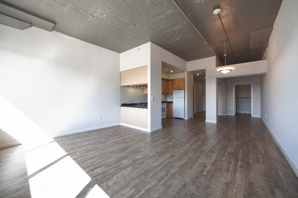 an empty living room with a kitchen in the background