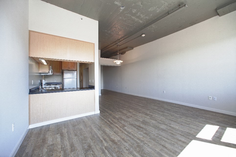 an empty living room with a kitchen in the corner
