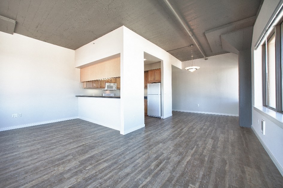 an empty living room with a kitchen in the corner