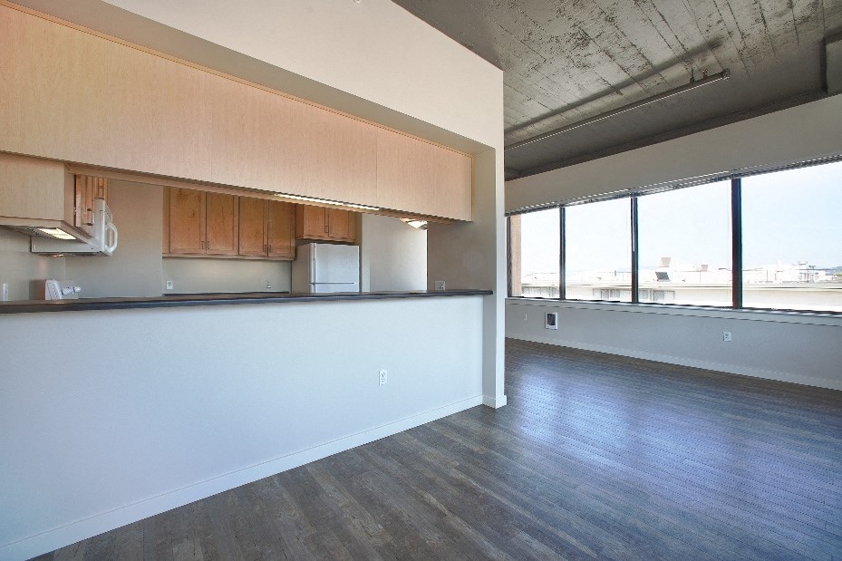an empty living room with a kitchen and a large window