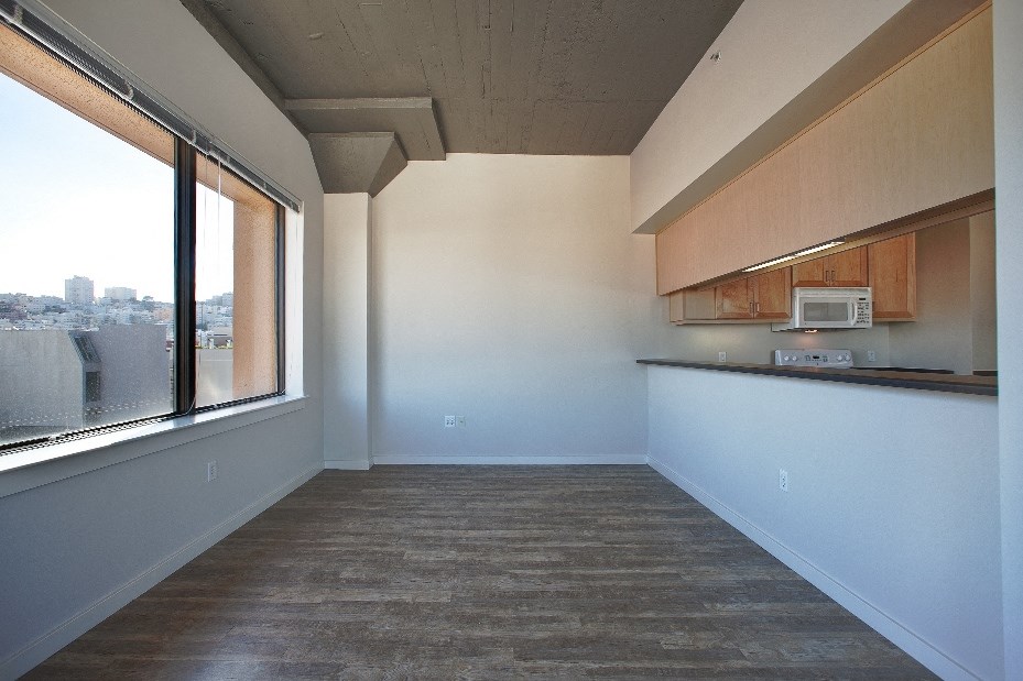 an empty living room with a large window and a kitchen