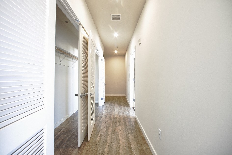 a hallway with white walls and wood floors and a closet